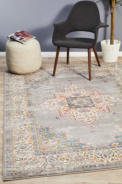 Babylon Grey Rug styled in a modern living room with chair, poufs, and plant, showcasing its detailed border and central medallion.
