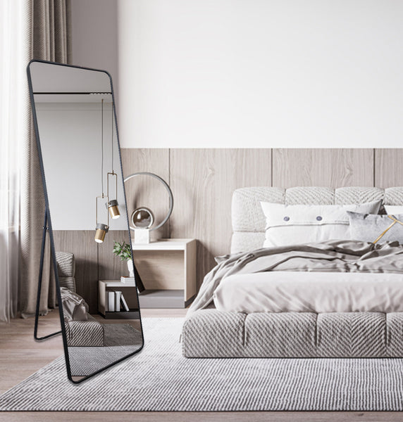 Free standing black rectangle mirror styled in bedroom interior with grey tones and soft lighting.