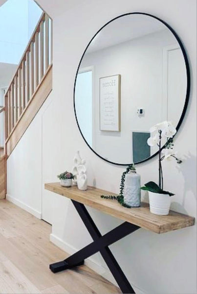 Black round mirror styled above wooden hallway console table with décor accents