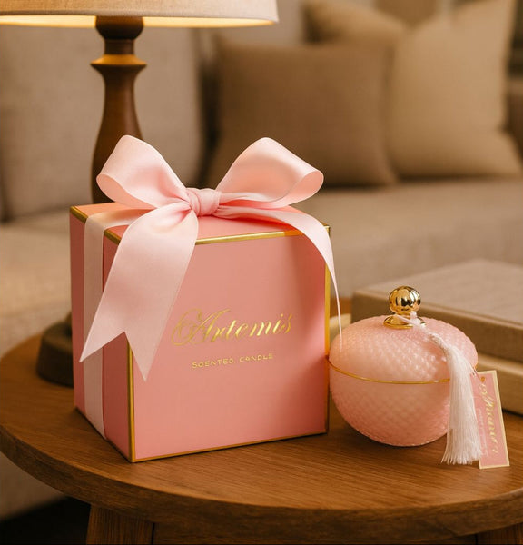 Pink gift box with a bow and a matching pink candle on a wooden table.