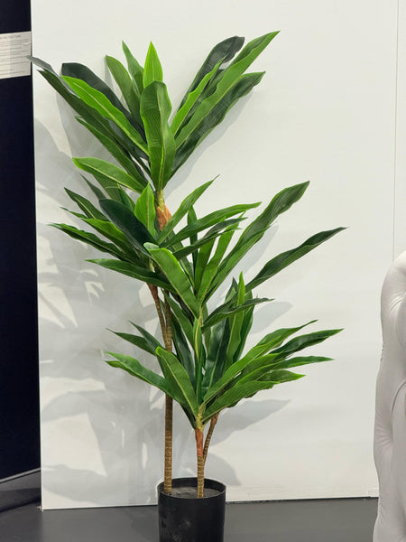 Tall artificial tropical plant with vibrant green foliage in a black pot, displayed indoors.