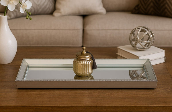 Decorative mirror silver tray on a wooden coffee table with a vase, books, and decorative ball.