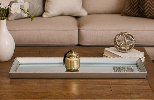 Decorative Mirrored Silver Tray on a coffee table with a vase, books, and a small ball in front of a beige sofa.