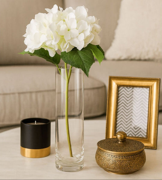 Decorative setup with a vase of white flowers, black candle, gold box, and picture frame on a table.