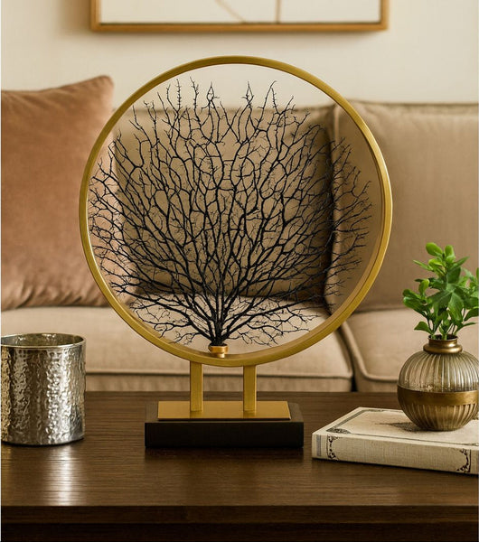 Decorative piece with a gold frame and black tree-like design on a table in a living room setting.