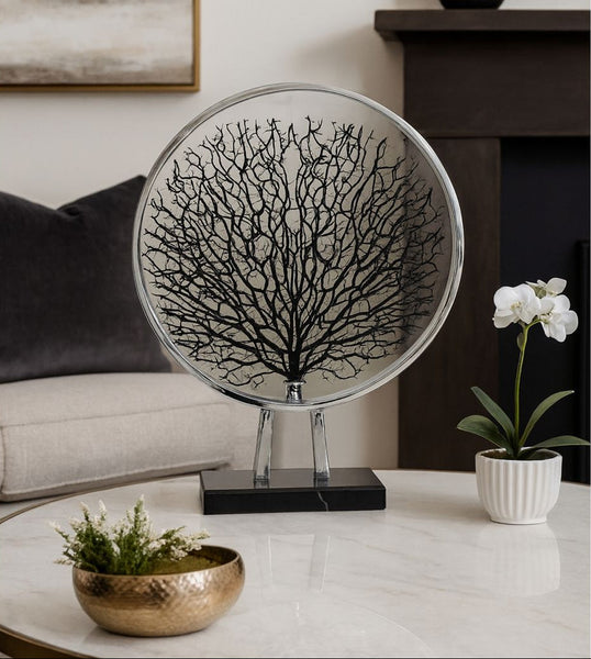 Decorative silver round piece with black tree design on a white surface