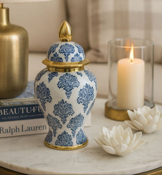 Decorative ceramic jar with blue floral patterns on a marble surface with candles and books in the background.