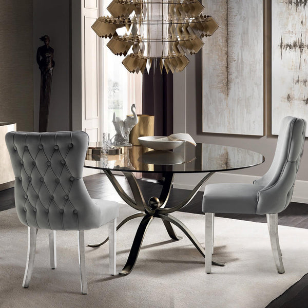 Light grey velvet Paris dining chairs with silver legs styled beside a glass dining table.