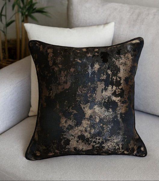 Decorative pillow with a black and gold distressed pattern on a light-colored sofa.