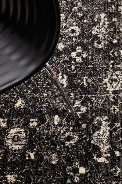 Detailed view of charcoal rug pattern beneath modern black chair.