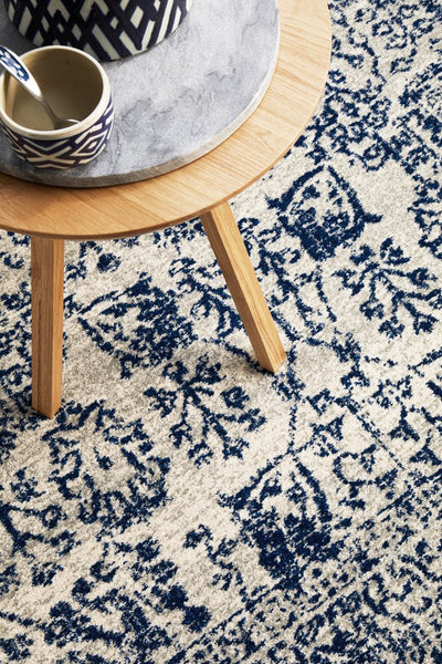 Close-up of ivory rug featuring bold navy motifs placed under round wooden side table.
