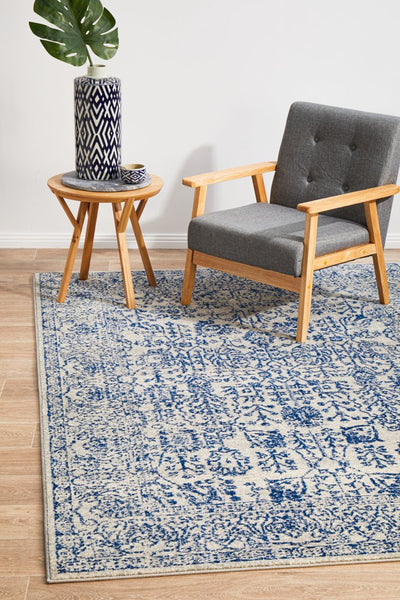 Navy patterned rug styled with grey armchair and wooden side table in a cozy space.