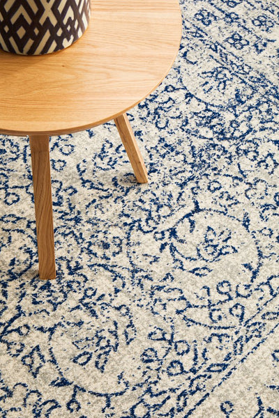 Close view of navy floral rug pattern under wooden side table, showing intricate weaving details.