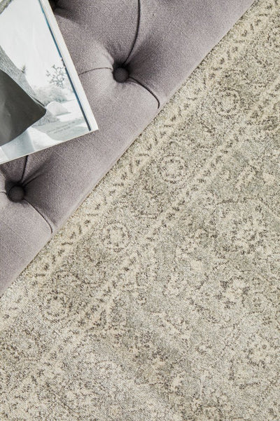 Soft textured rug in silver tones placed near tufted sofa, showcasing detailed woven floral patterns.