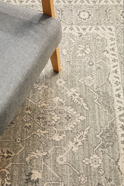 Close view of silver rug corner with intricate design placed under a modern wooden chair.