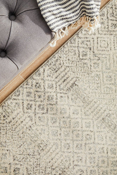 Close-up of Evoke 265 Grey Rug near sofa with striped throw, highlighting soft grey pattern.