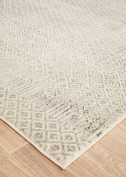 Corner view of Evoke 265 Grey Rug on wooden flooring, showing textured distressed finish.