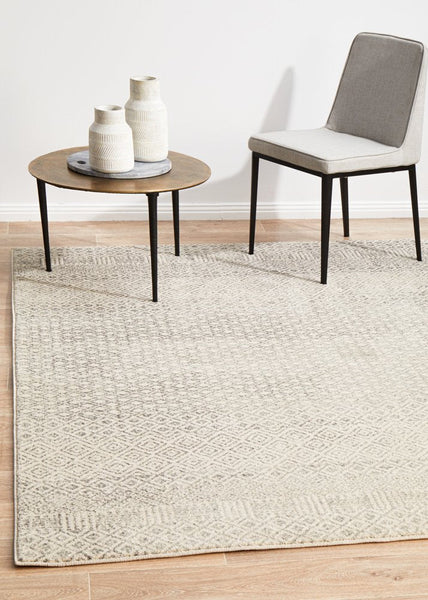 Evoke 265 Grey Rug styled with a chair and round table, adding elegance to a modern living room.