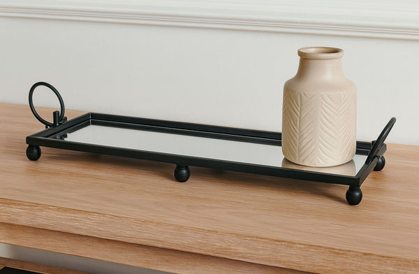Black metal mirror tray with a beige vase on a wooden surface