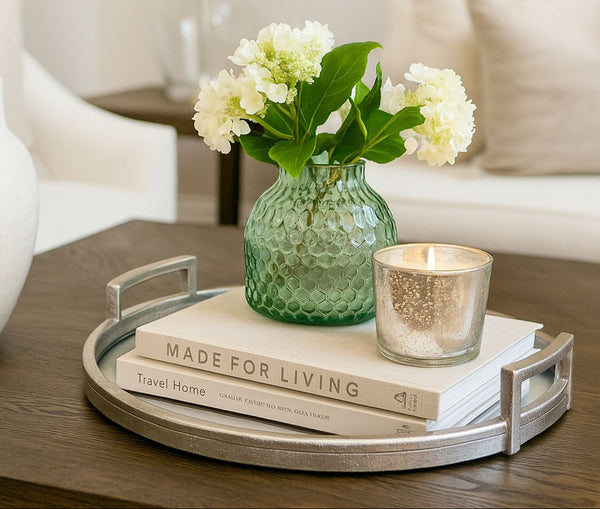 Decorative mirror silver large tray with books, a candle, and a vase of flowers on a table.