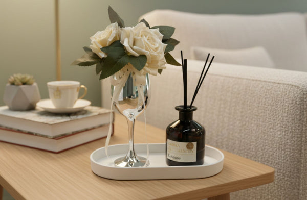 Decorative setup with flowers in a champagne glass, and a diffuser on a table.