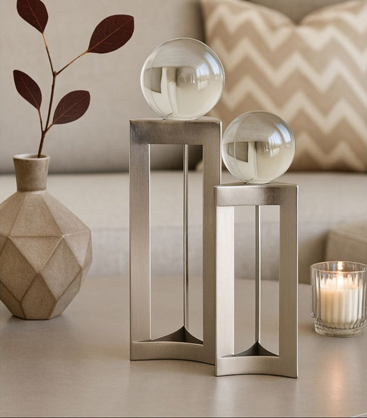 Decorative metallic table stand with glass shades on a light surface, next to a vase and candle.