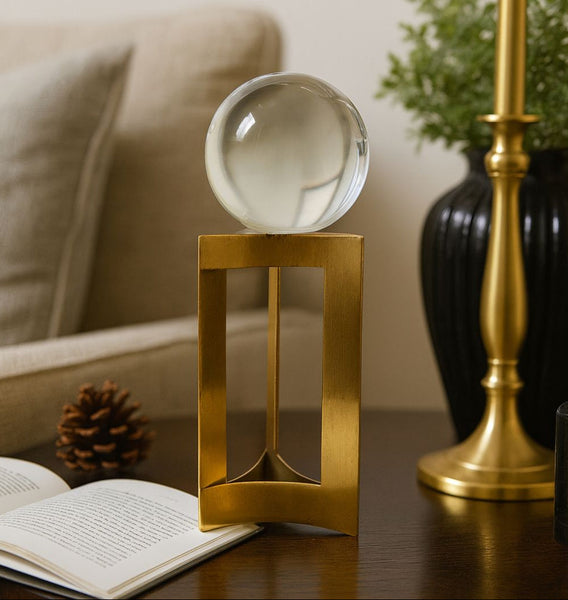 Decorative glass sphere on a gold stand with a book and plant in the background
