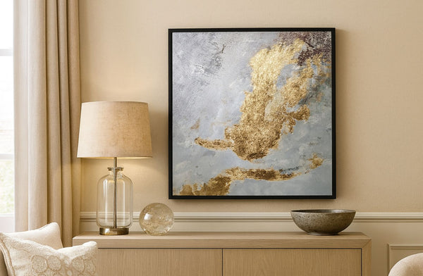 Framed abstract art piece with a hint of gold on a wall with a lamp and decorative bowls below.
