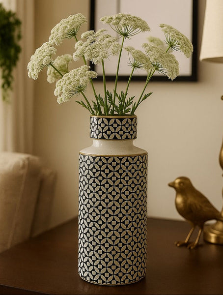 Decorative vase with patterned design containing white flowers on a wooden surface.