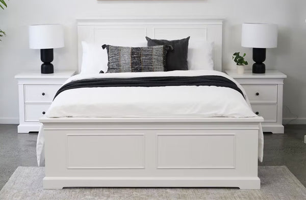 Hamptons white bed frame styled with black lamps, cushions and matching bedside tables in a bright room.