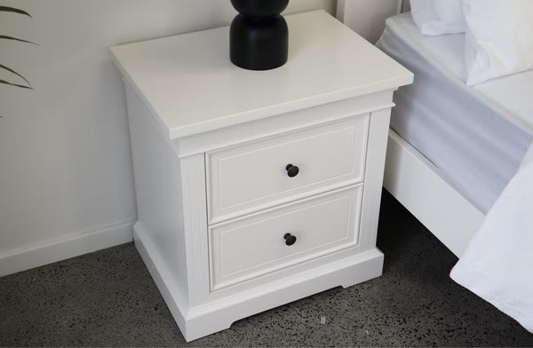 Hamptons white bedside table with two drawers styled beside a bed in a modern room.