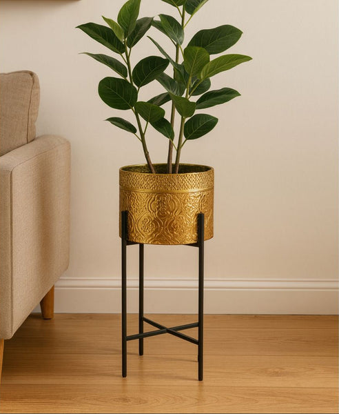 Gold decorative planter with a plant on a black stand in a room with beige walls and wooden floor.