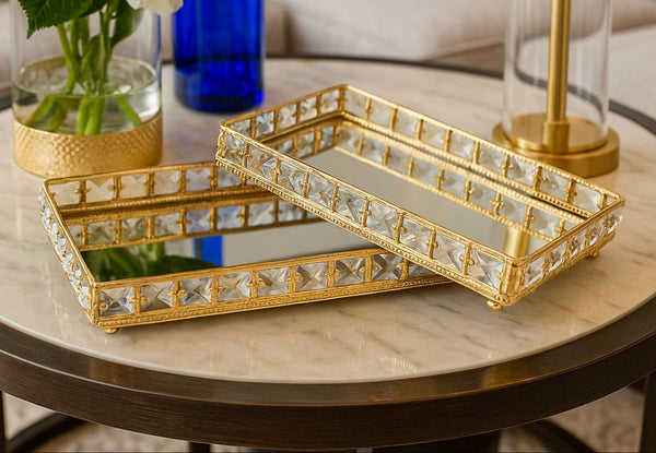 Two gold and crystal decorative mirror trays on a marble table.