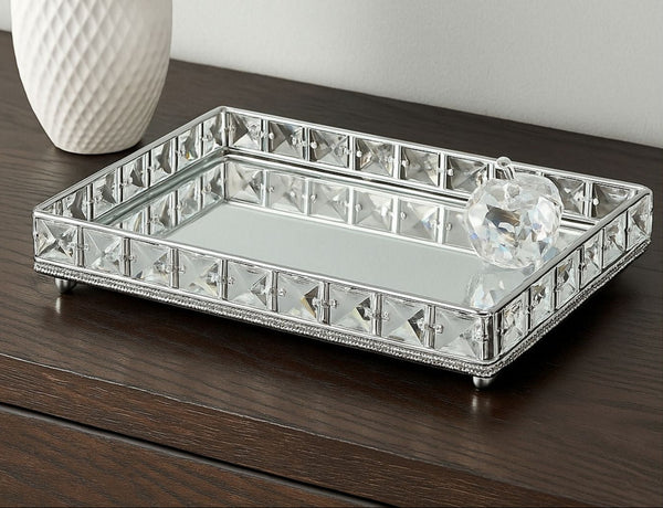 Decorative crystal mirror tray on a wooden surface with a white vase in the background