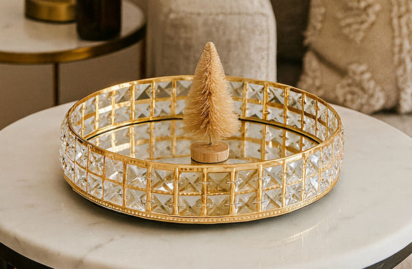 Decorative gold mirror tray with a small Christmas tree on a marble surface