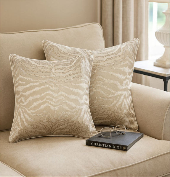 Beige pillows with patterns on a couch with a book and glasses in a living room setting