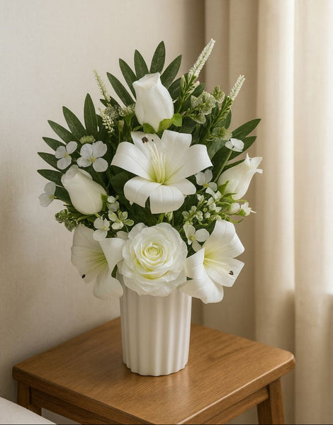 Bouquet of white flowers in a vase on a wooden table against a neutral wall.