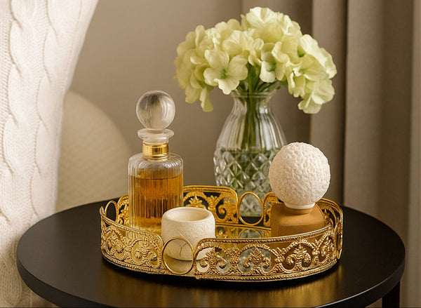 Decorative gold oval tray with a perfume bottle, candle, and vase of flowers on a table.