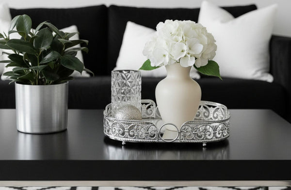 Decorative oval silver tray with a vase of white flowers, a glass, and a potted plant on a table.