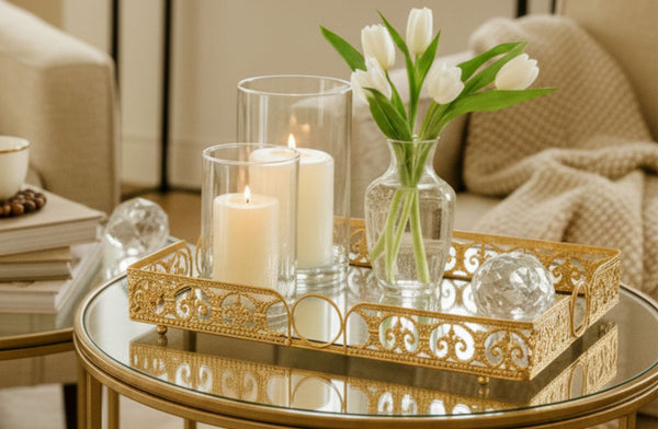 Decorative rectangle table setting with candles, a vase of tulips, and a gold tray on a glass table.
