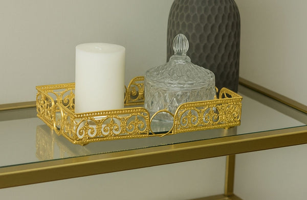 Decorative gold rectangle tray with a candle and glass container on a reflective surface.