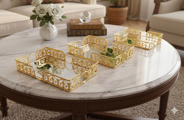 Set of gold decorative rectangle trays on a marble coffee table with a vase and books in the background.