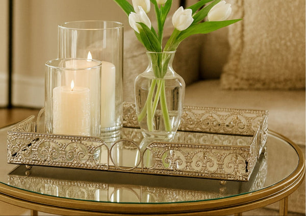 Decorative rectangle mirror tray with candle, glass vase with flowers, and books on a table.