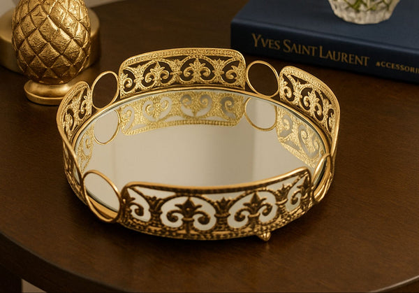 Decorative gold round mirror trayl on a wooden surface with 'Yves Saint Laurent' book in the background.