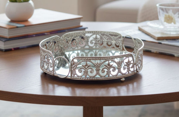 Decorative round silver tray on a wooden table with books and a plant in the background