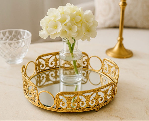 Decorative round gold tray with a vase of white flowers on a marble surface.