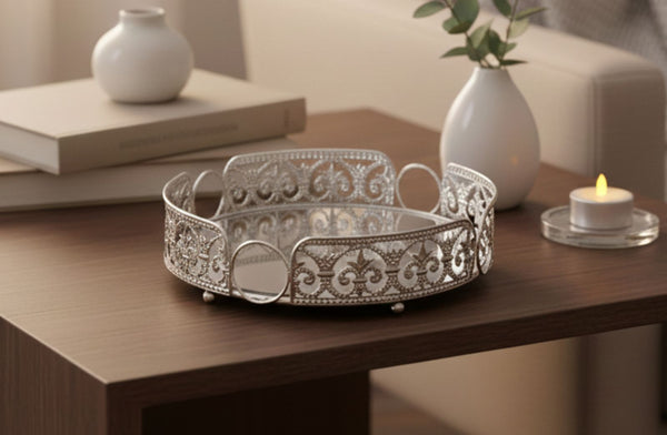 Decorative silver round tray on a wooden table with a candle and books in the background