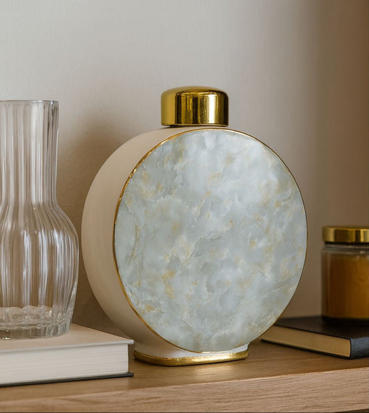 Decorative jar with gold base and white textured shade on a shelf.