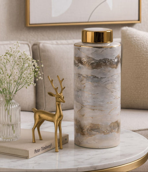 Decorative cylindrical vase with gold accents on a marble table in a living room setting.