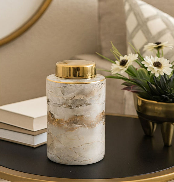 Decorative jar with gold lid on a table next to books and a plant